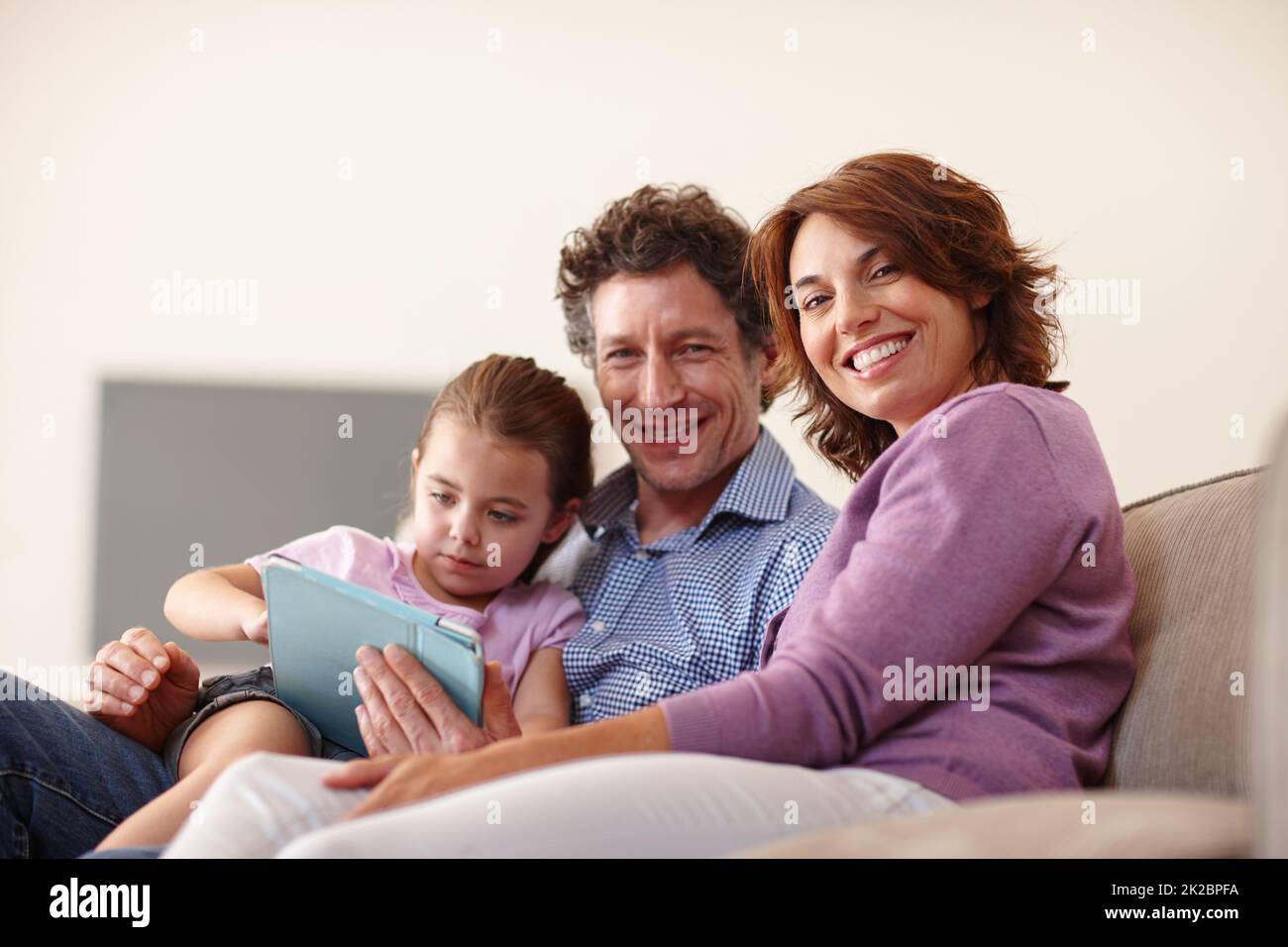 La famiglia è un piccolo mondo creato dall'amore. Scatto di una bambina con un tablet digitale bianco seduto con i genitori. Foto Stock
