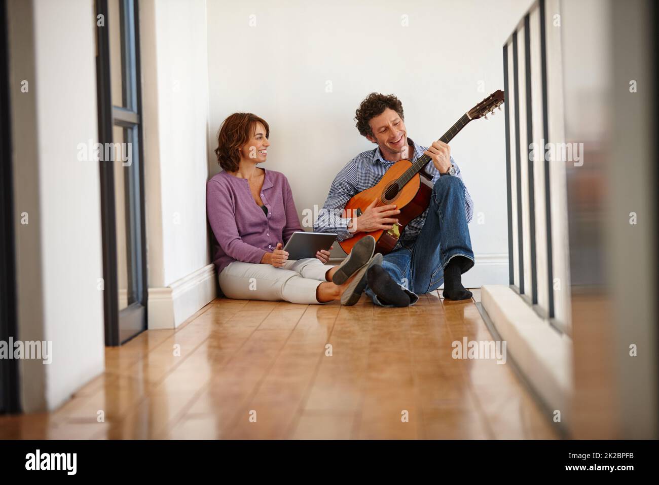 È un talento felice di sapere come giocare. Scatto di una donna con il suo tablet digitale mentre suo marito suona la chitarra. Foto Stock