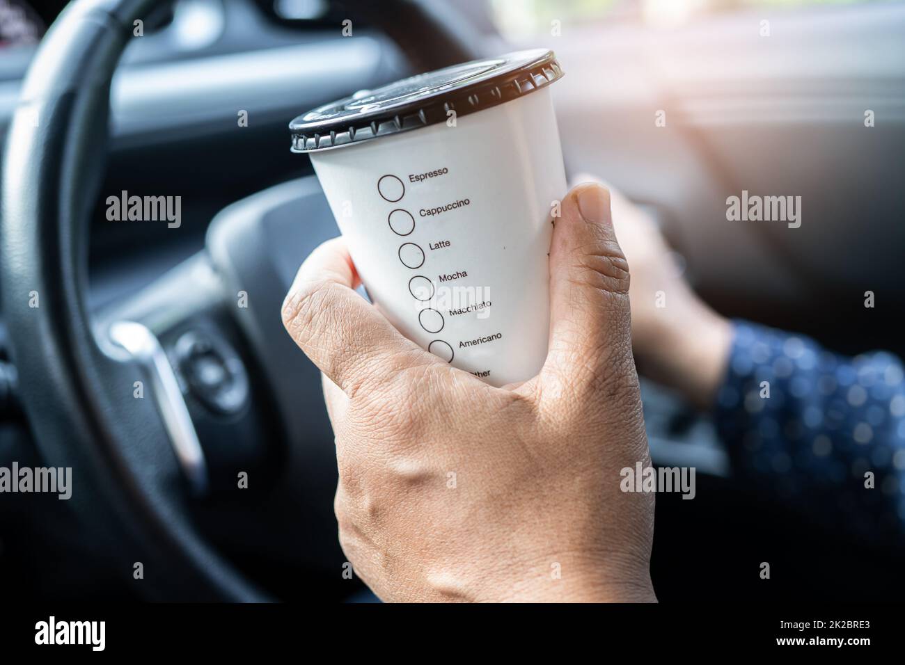 Signora asiatica che tiene il cibo caldo della tazza di caffè per bere in auto, pericoloso e rischio di un incidente. Foto Stock