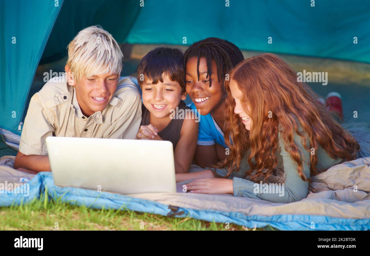 Sempre connessi, ovunque si trovino: Tecnologia moderna. I bambini si divertono a usare un computer portatile mentre si accamparono in una tenda. Foto Stock