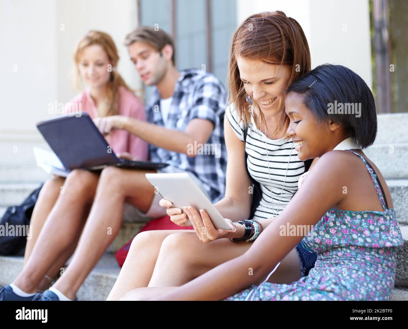 Adolescenti tecnologici. Giovani adolescenti che guardano i loro notebook e tablet digitali mentre socializzano all'aperto. Foto Stock