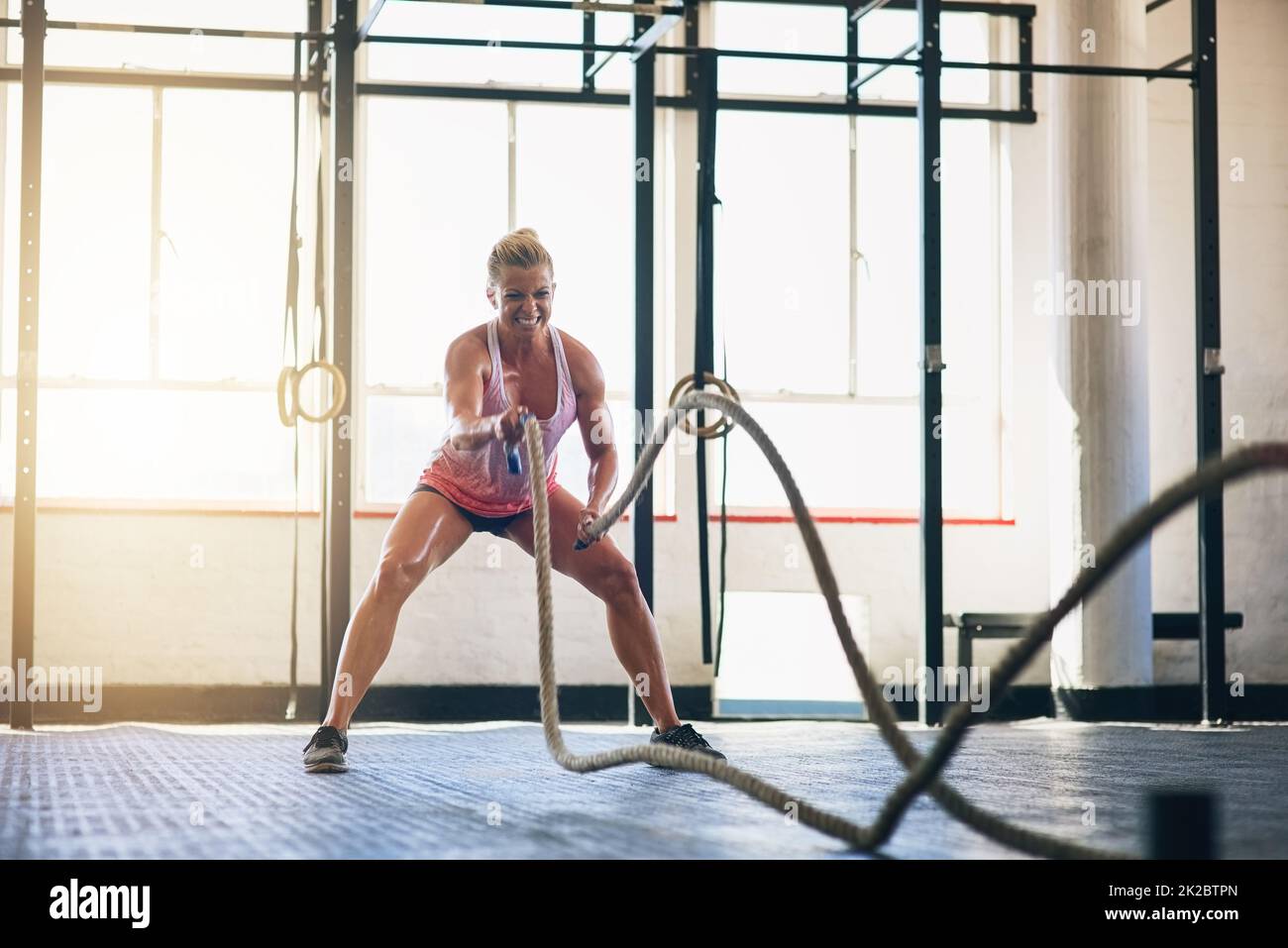 Youre soltanto ottenere più forte. Shot di una giovane donna sportiva che si allena con corde pesanti in palestra. Foto Stock