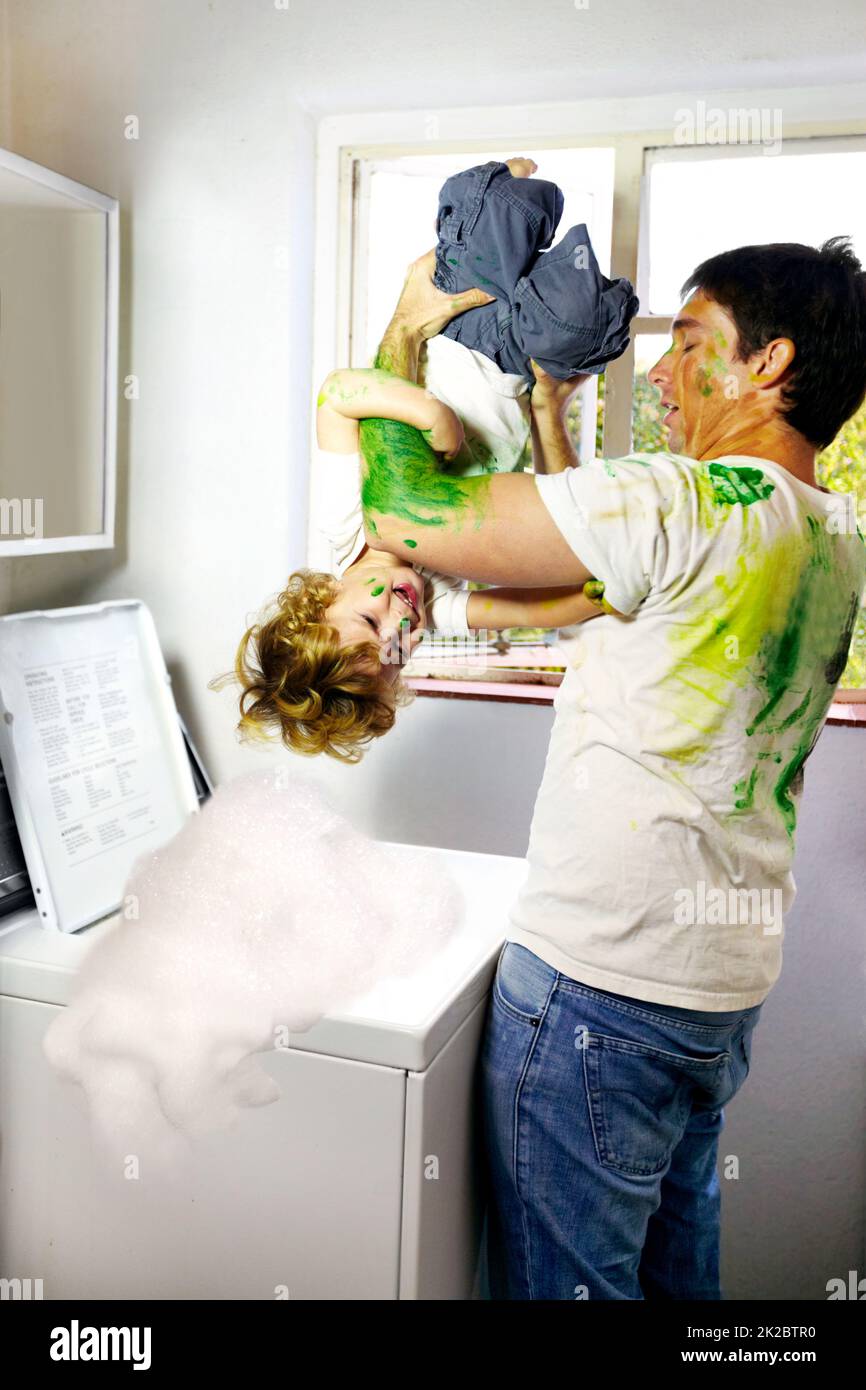 Parenting difettoso. Padre coperto di vernice che tenta di mettere il suo bambino nella lavatrice. Foto Stock
