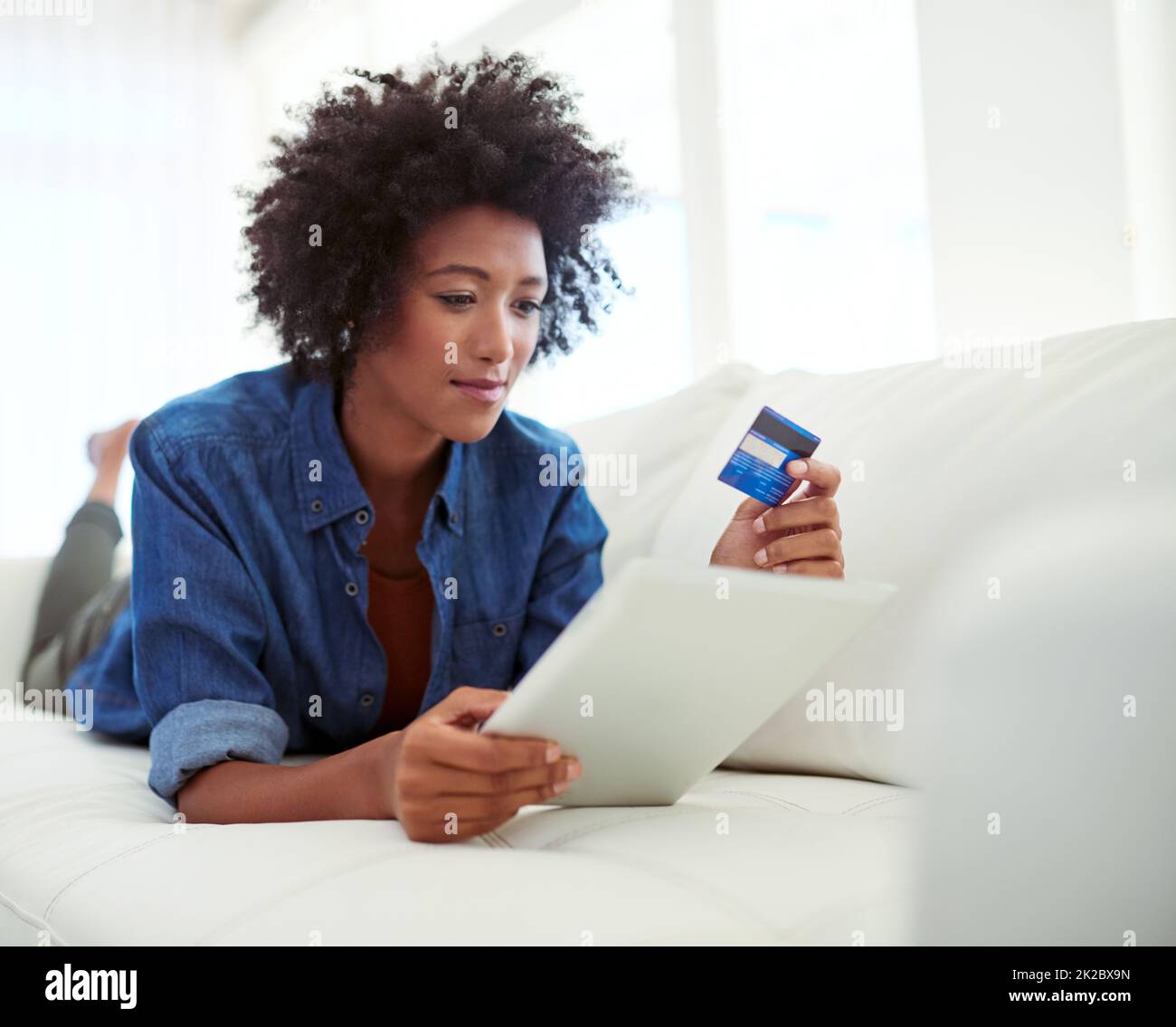 Confortevole consumismo. Shot di una giovane donna attraente shopping online dalla comodità di casa. Foto Stock