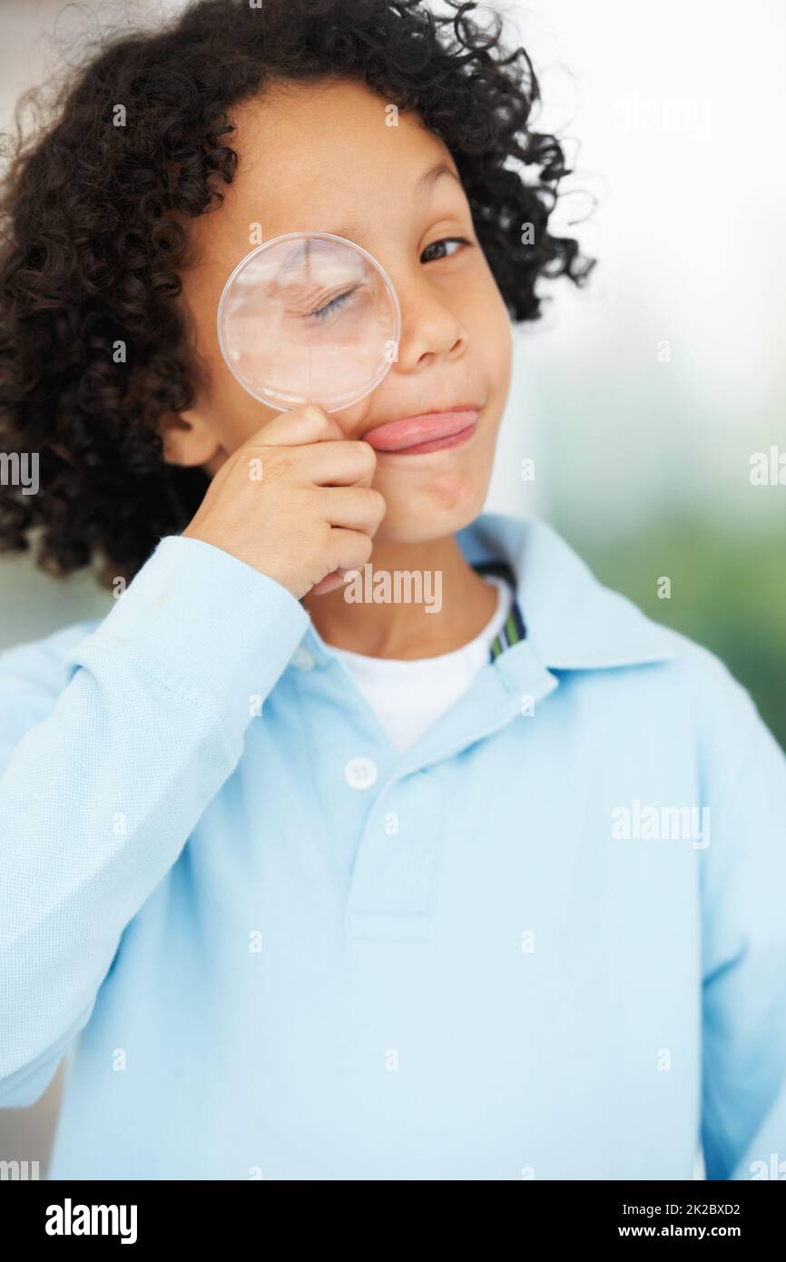 HES una mente curiosa. Ritratto di un ragazzo carino che guarda mentre tiene una lente d'ingrandimento sopra l'occhio chiuso. Foto Stock