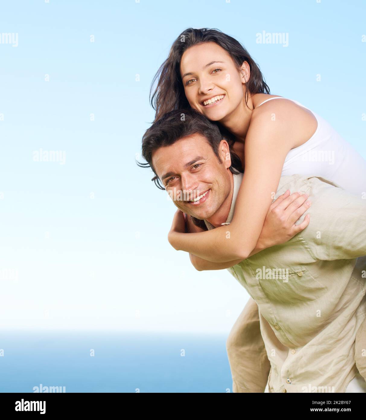 La porta a vedere la vista. Un giovane piggybacking la sua ragazza con una vista dell'oceano sullo sfondo. Foto Stock