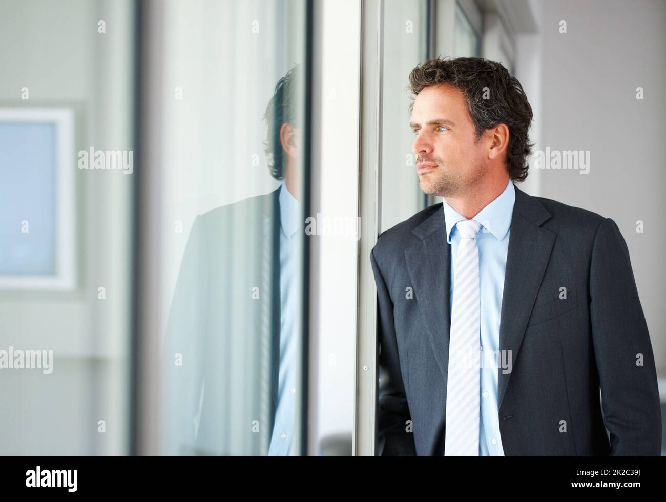 Uomo d'affari che guarda fuori attraverso la porta. Uomo d'affari intelligente di mezza età che guarda fuori attraverso una porta di vetro. Foto Stock