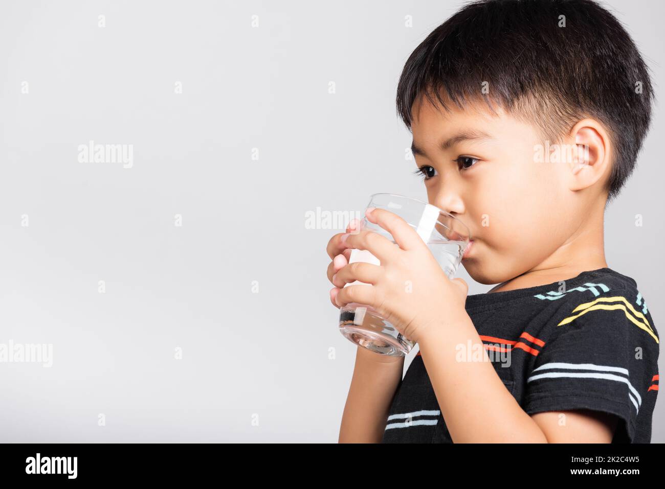 Bambino piccolo carino ragazzo di 5-6 anni sorriso bere acqua fresca dal vetro in studio ripresa isolato Foto Stock