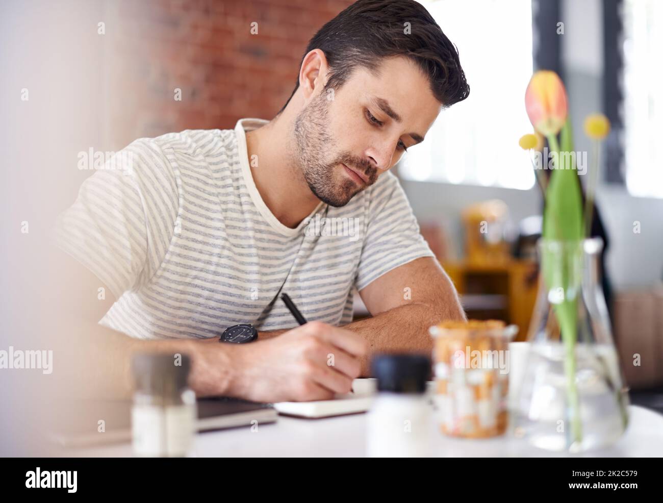 Il materiale di scrittura. Scatto di un bel giovane uomo che scrive in un taccuino mentre si siede ad un tavolo del ristorante. Foto Stock