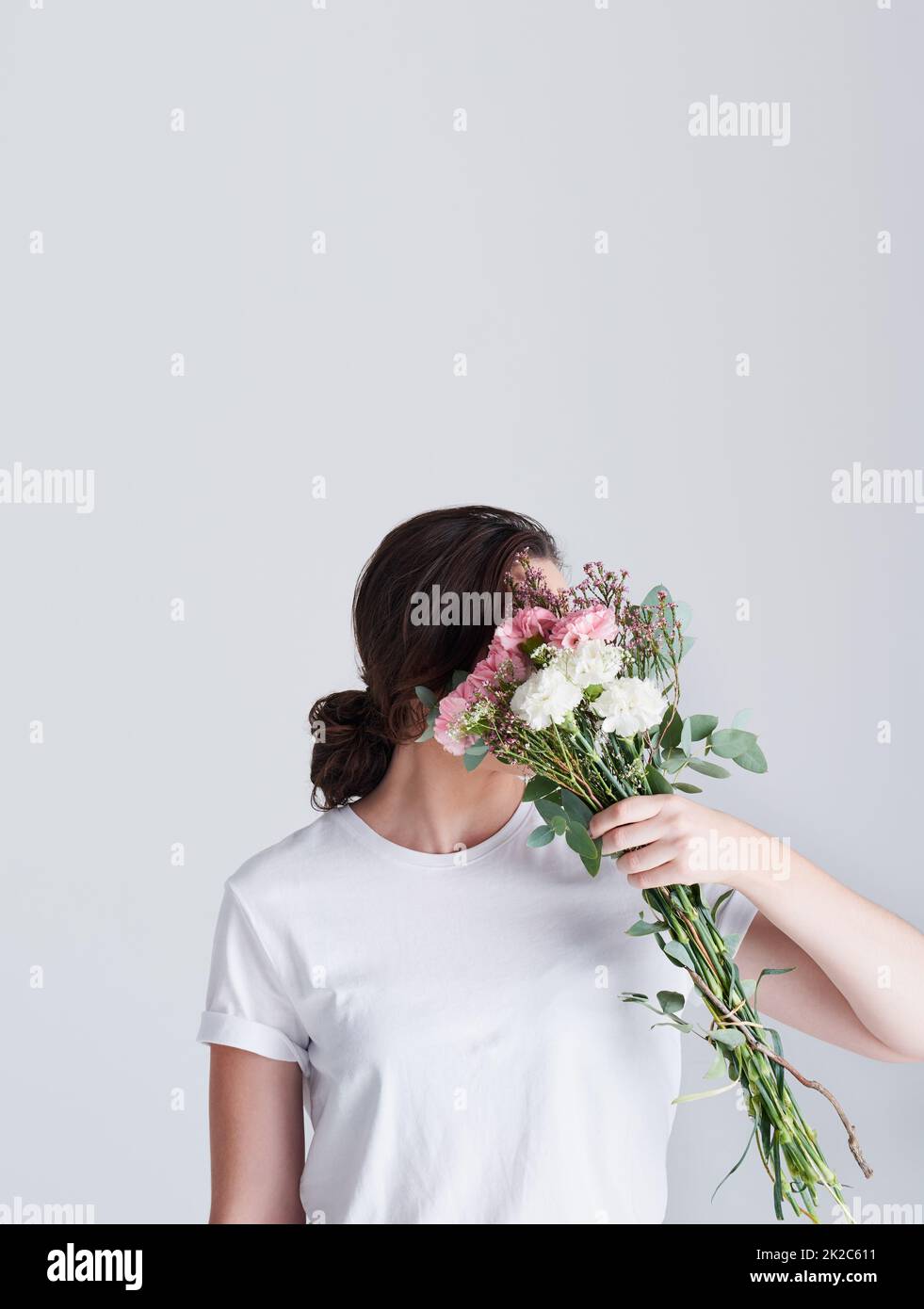 C'è purezza nei fiori. Studio girato di una donna irriconoscibile coprendo il suo viso con fiori su sfondo grigio. Foto Stock