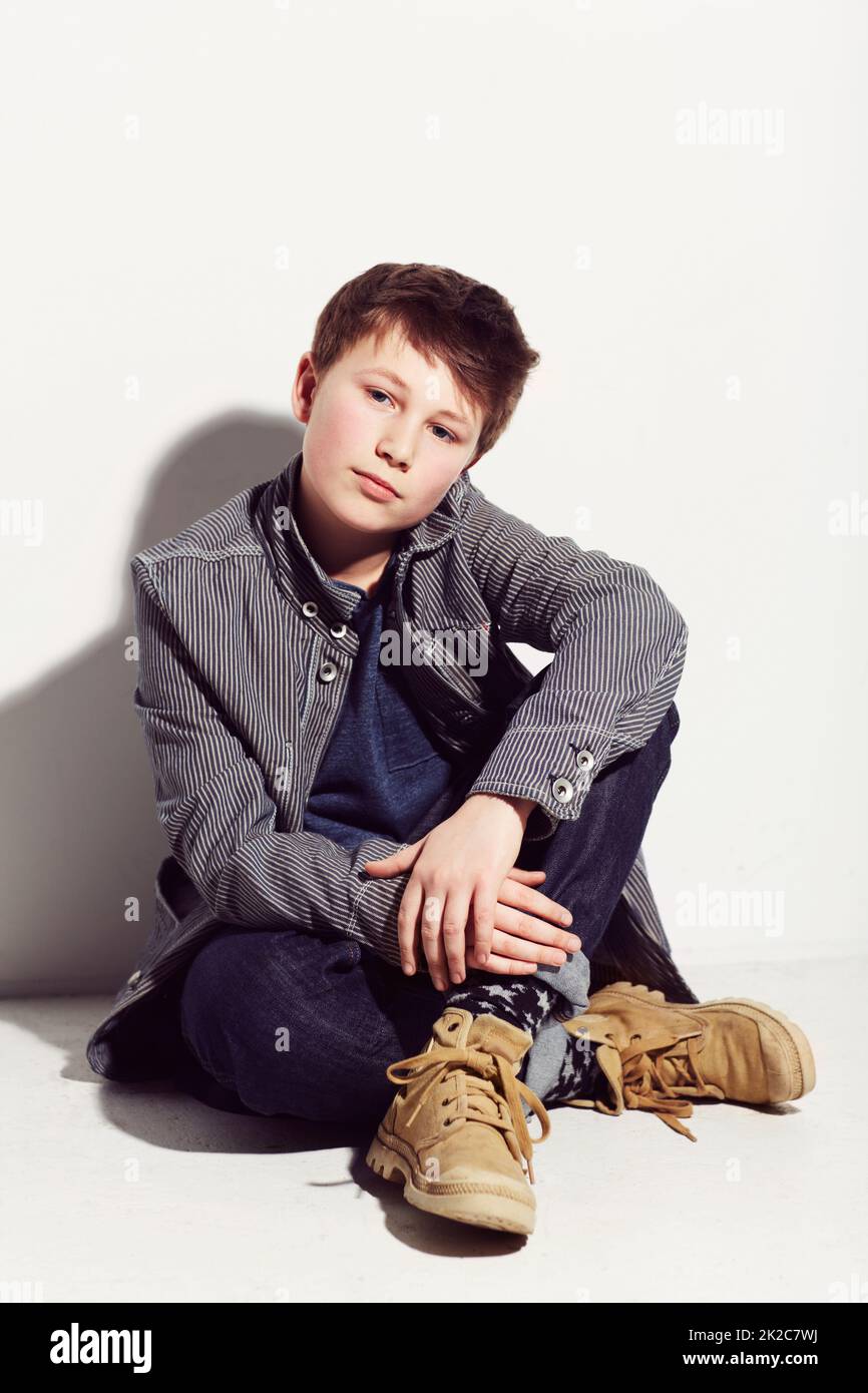 Stile rilassato e semplice. Ragazzo giovane adolescente seduto su sfondo bianco. Foto Stock