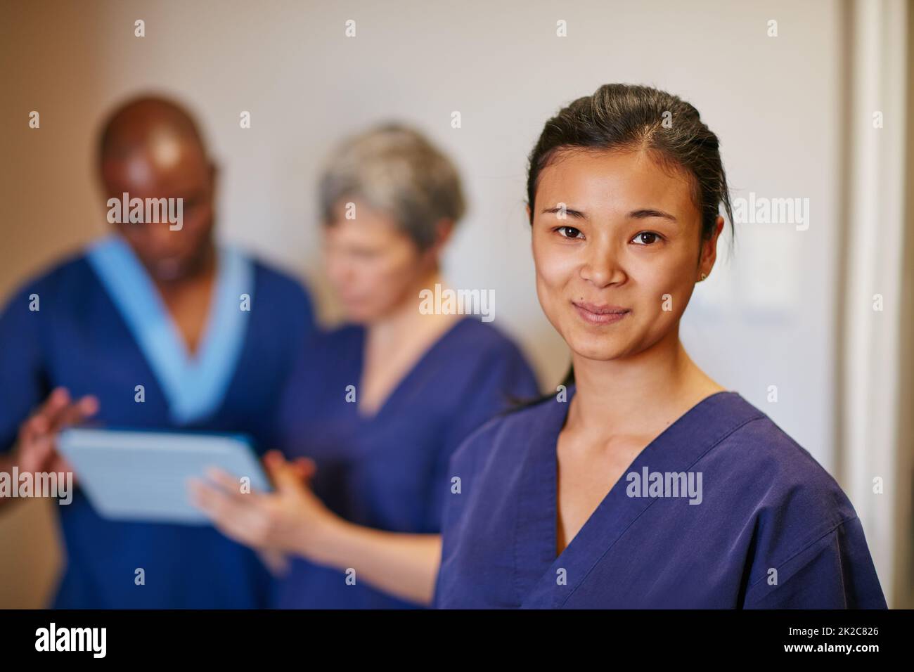 Aiutare le persone è così appagante. Ritratto corto di una nutrice in piedi in un ospedale con i suoi colleghi in background. Foto Stock
