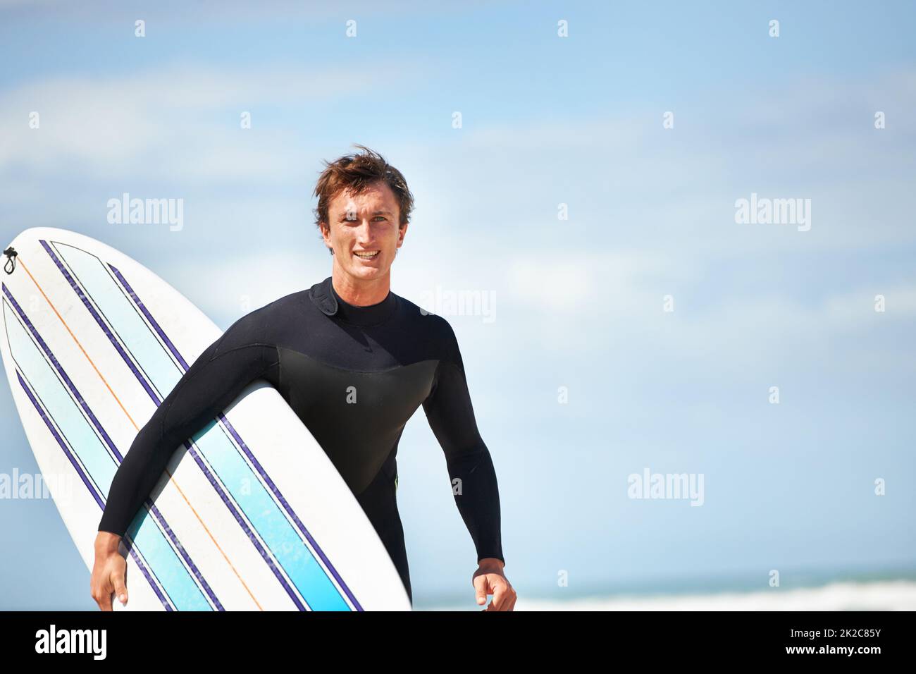 È solo io e la mia tavola da surf. Ritratto di un giovane surfista in spiaggia in una giornata di sole. Foto Stock