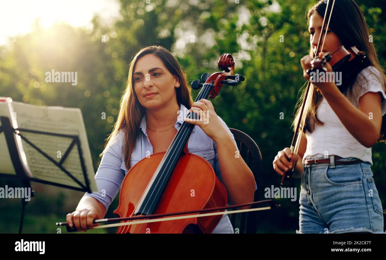 Ha insegnato a sua figlia come giocare. Scatto corto di una madre e di una figlia che suonano strumenti musicali insieme nel cortile. Foto Stock