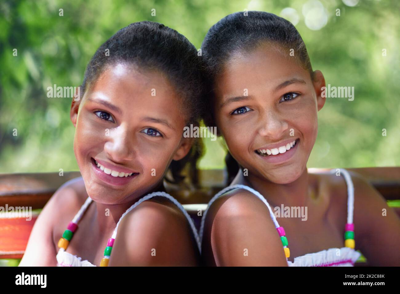Due di un genere. Ritratto corto di due sorelle gemelle sedute su una panchina del parco. Foto Stock