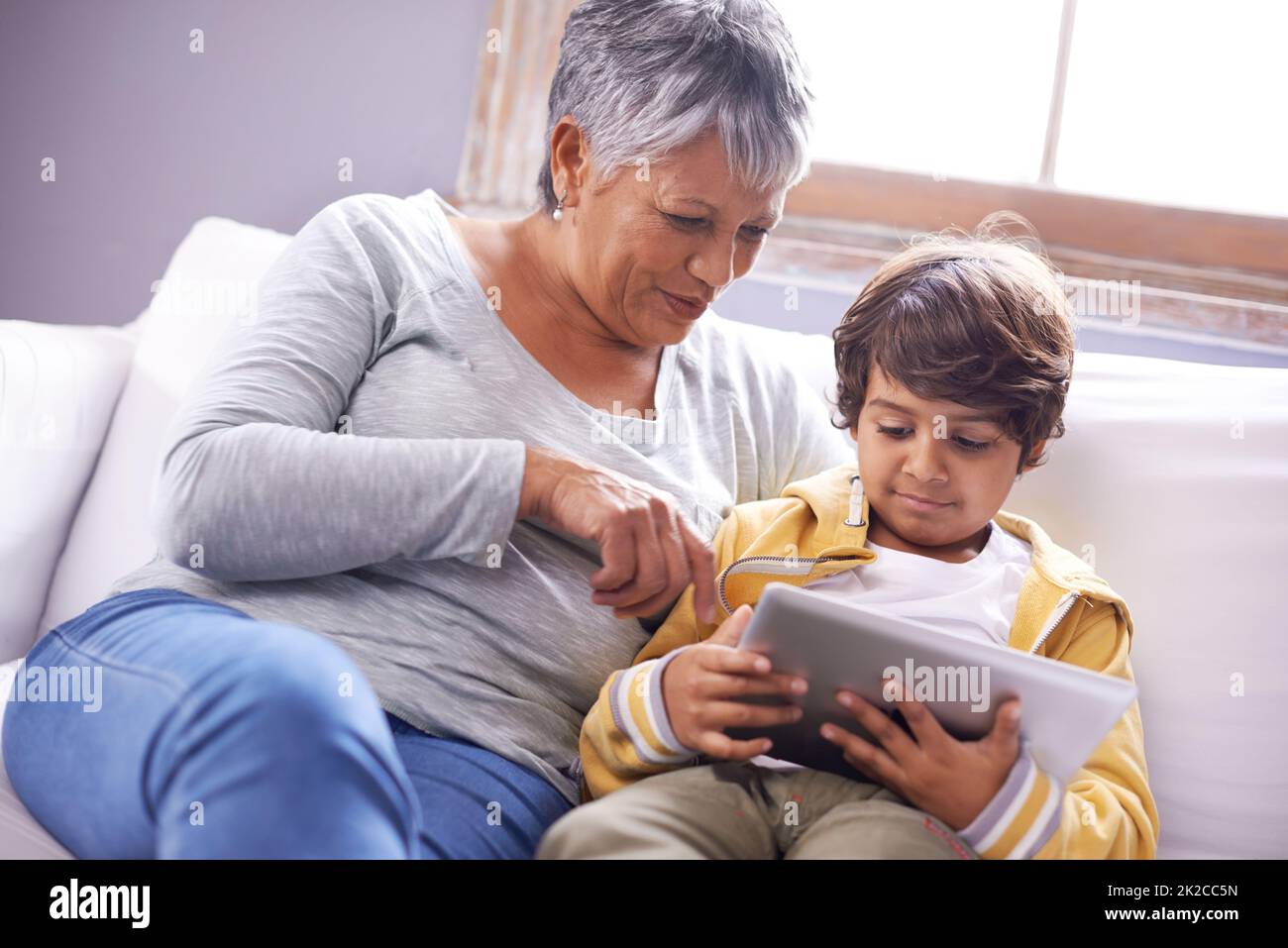 Dare alla nonna una lezione online. Scatto di una nonna e di un nipote seduti a casa utilizzando un tablet digitale insieme. Foto Stock