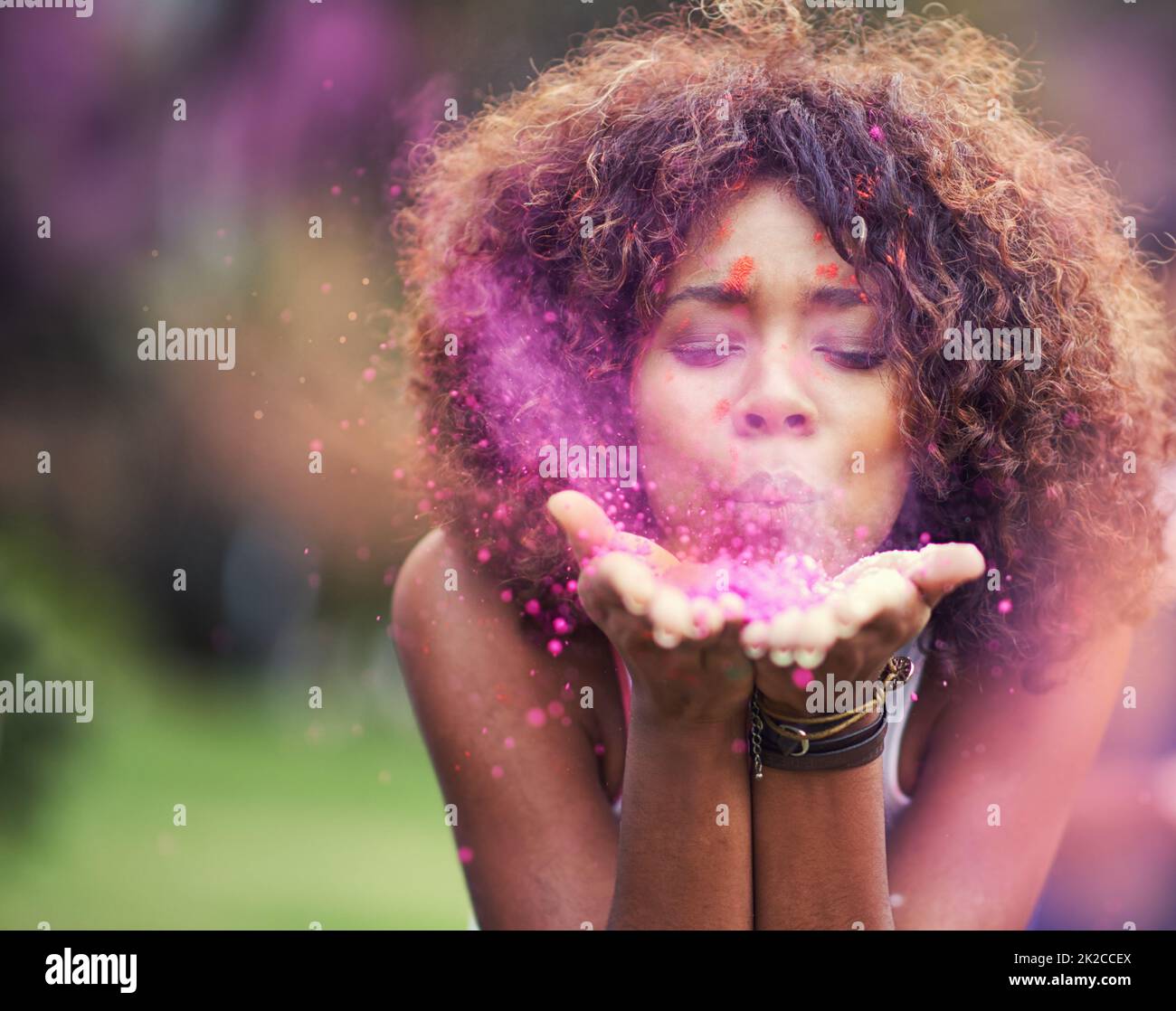 Dipingere il mondo rosa. Scatto di una giovane donna attraente che soffia la polvere di vernice viola alla macchina fotografica. Foto Stock