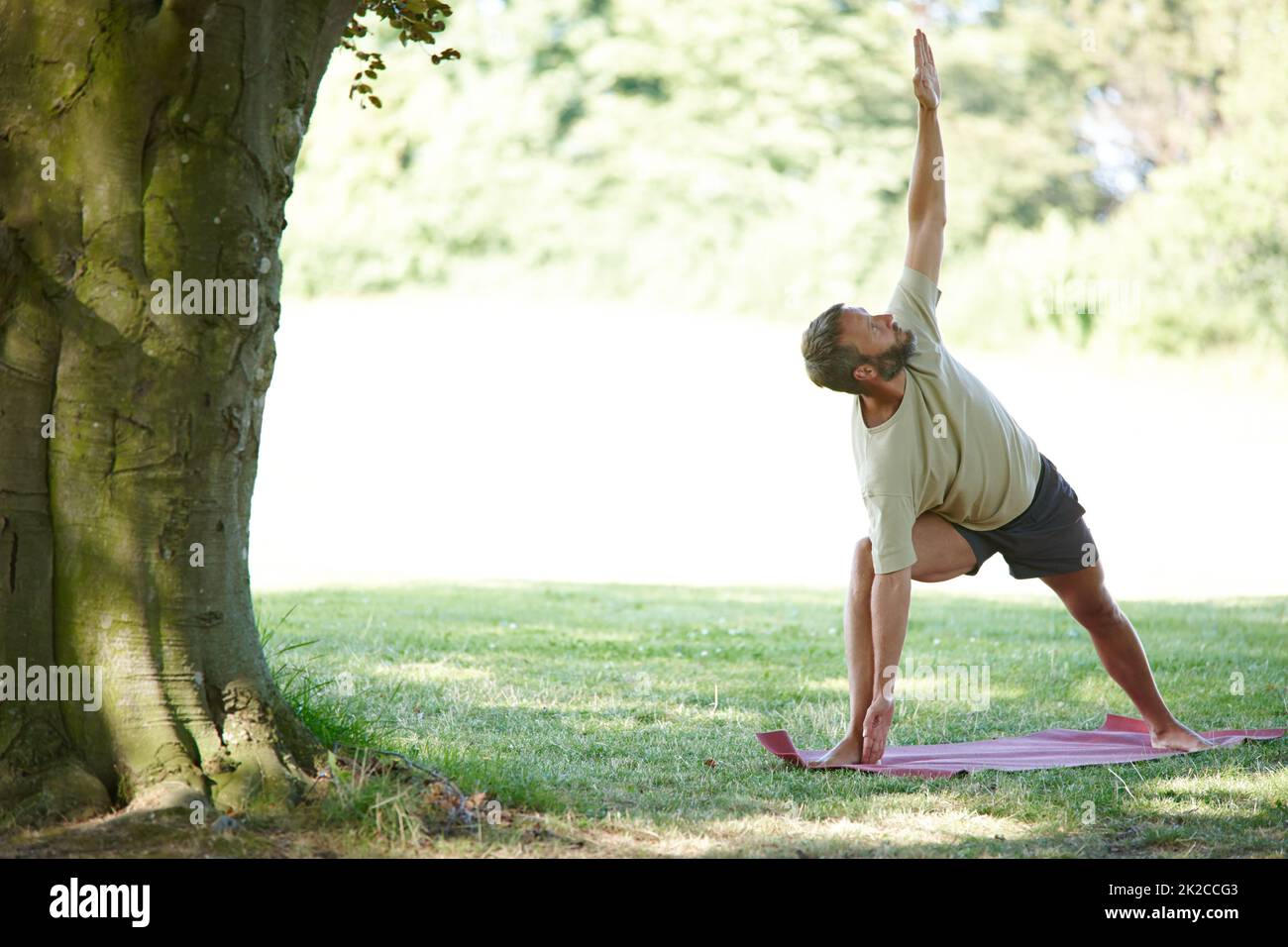 Concentratevi sul fatto di essere un triangolo. Scatto a tutta lunghezza di un bell'uomo maturo che fa yoga all'aperto. Foto Stock
