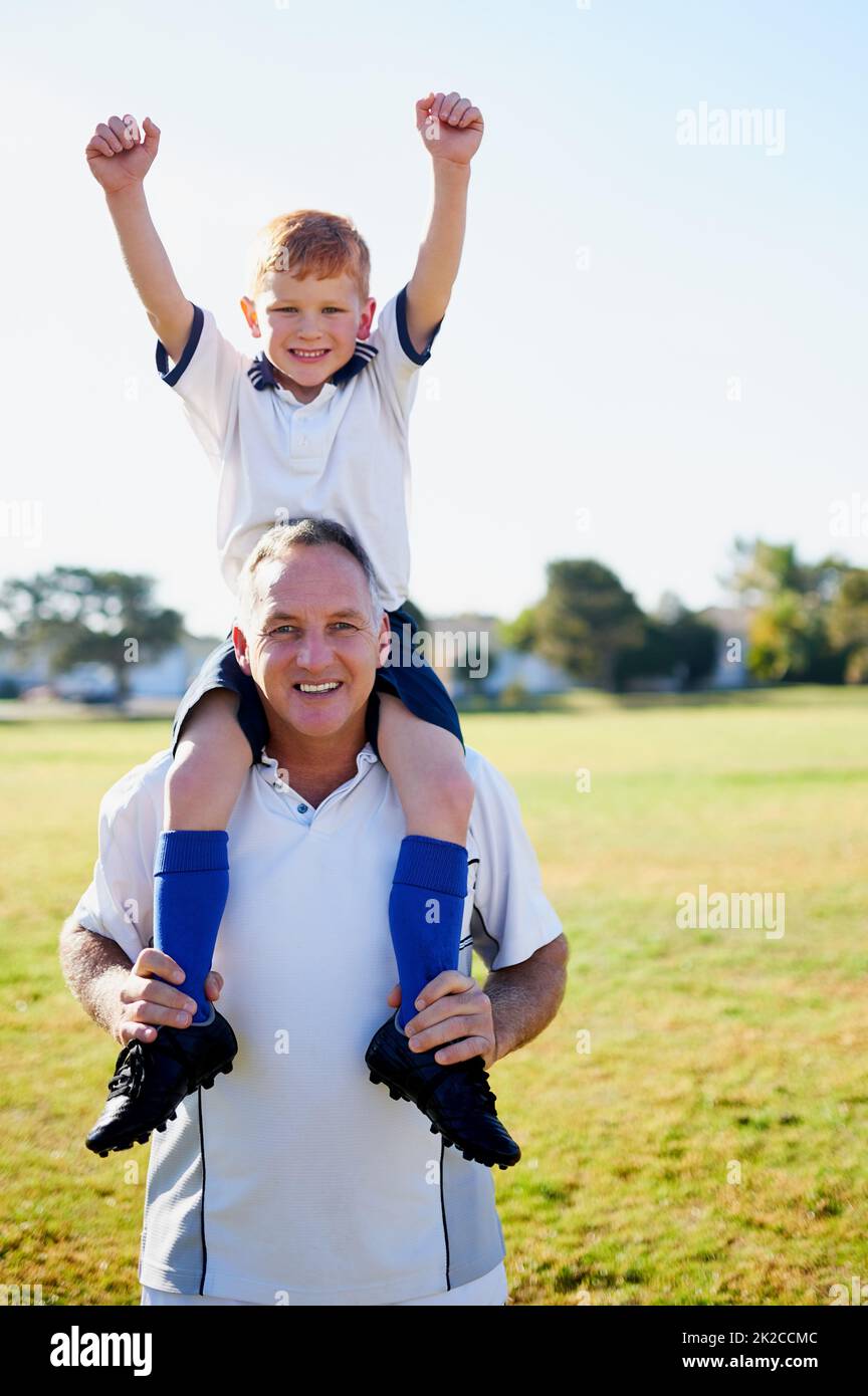 Papà è il miglior allenatore. Ritratto di un padre che porta il figlio sulle spalle dopo una partita di calcio. Foto Stock