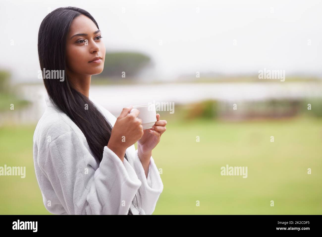 Vista panoramica. Una bella giovane donna che si gode una tazza di caffè indossando un accappatoio. Foto Stock