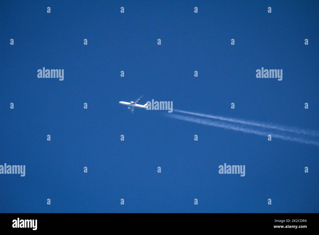 Un jet bianco, aereo passeggeri disegna due contraddii nel cielo blu. Foto Stock