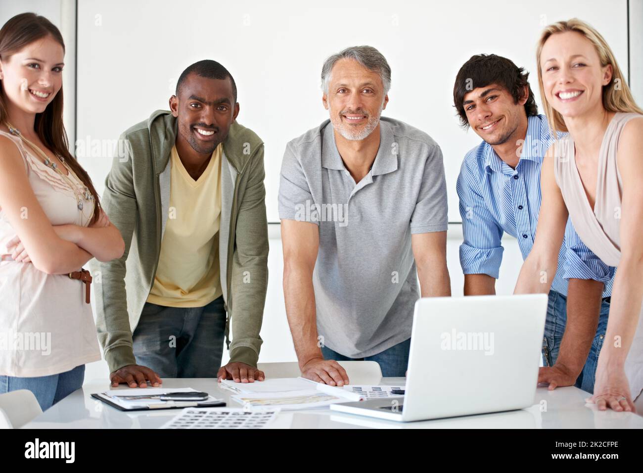 Nessun segreto per il nostro successo - lavoro di squadra. Un gruppo di uomini d'affari che si trovano dietro una scrivania con un computer portatile che sorride alla fotocamera. Foto Stock