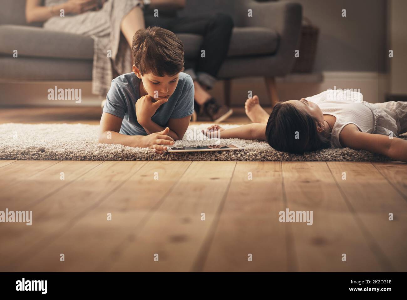 Il tempo di gioco è il tempo di apprendimento. Scatto di un adorabile fratello e sorella utilizzando un tablet digitale a casa con i loro genitori in background. Foto Stock