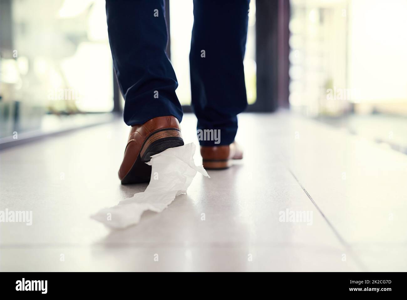 Trascinando il suo imbarazzo lungo. Primo piano di un uomo d'affari che cammina in un ufficio con carta igienica attaccata alla sua scarpa. Foto Stock