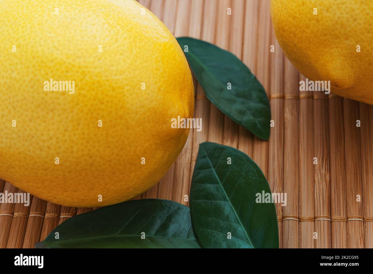 Primo piano di grandi limoni gialli e foglie verdi sul tappeto di bambù. Foto Stock