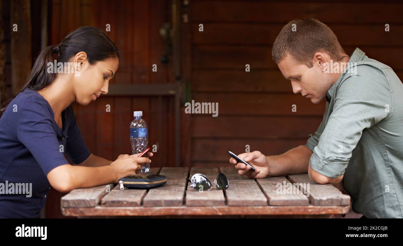 Distratto dalla tecnologia. Due giovani adulti che sono distratti dalla tecnologia mentre fuori su una data del caffè. Foto Stock