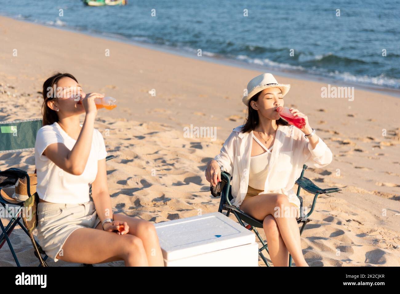 Amici felici con bevande in campeggio e ridere insieme in vacanze sulla spiaggia di sabbia vicino campeggio tenda vacanza al tramonto Foto Stock