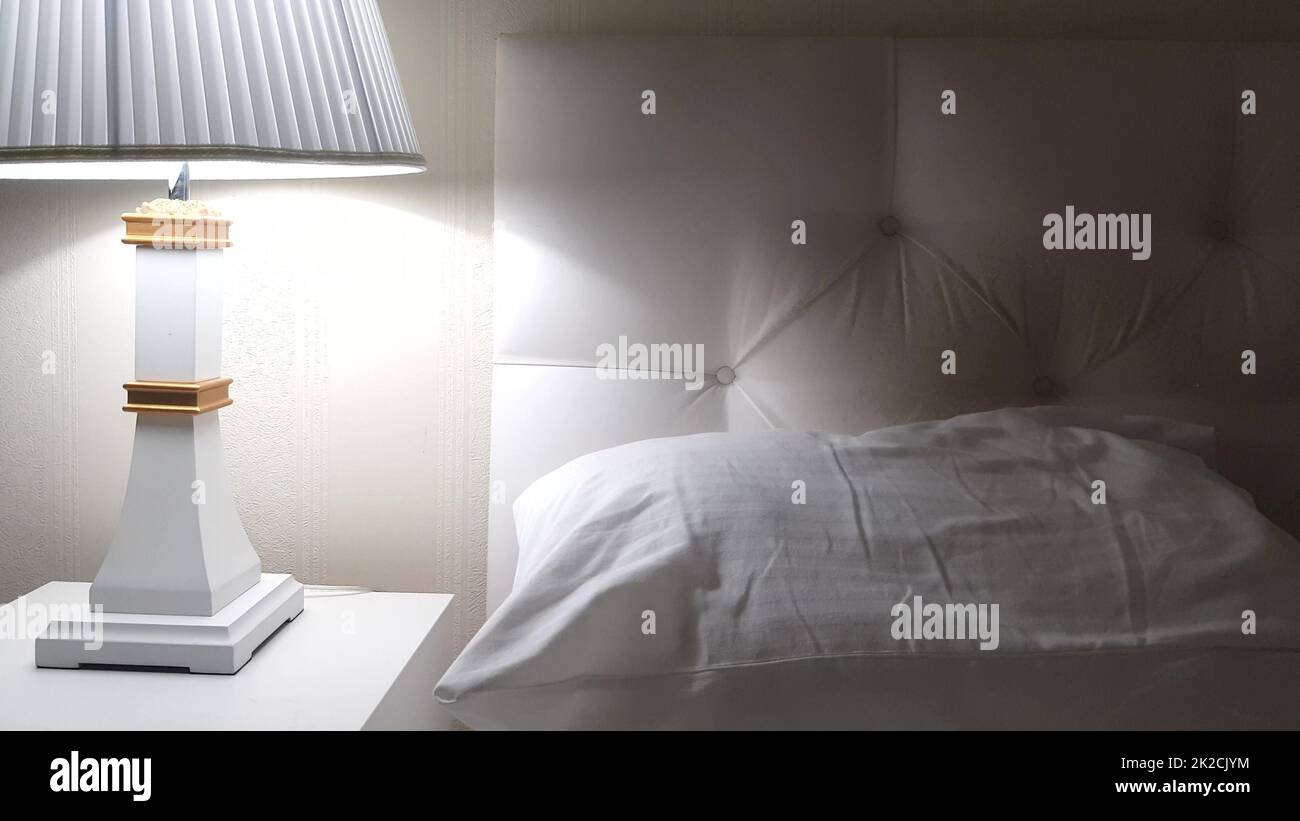 Letto d'albergo di lusso, preparazione per il letto, comodino con lampada e lenzuola bianche pulite sul letto con cuscino, sera Foto Stock
