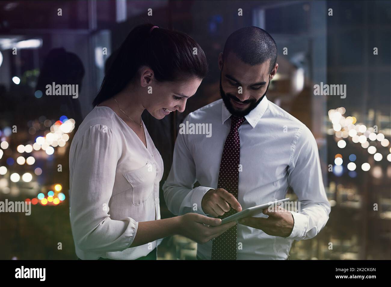 Immagine di due uomini d'affari che lavorano con un tablet digitale a tarda notte. Gli uomini d'affari della vita reale hanno girato sul posto. Poiché queste posizioni sono la cosa reale e non sparato in uno studio dell'ufficio, i livelli alti di ISO sono necessari a volte per interferire il momento. La È Foto Stock
