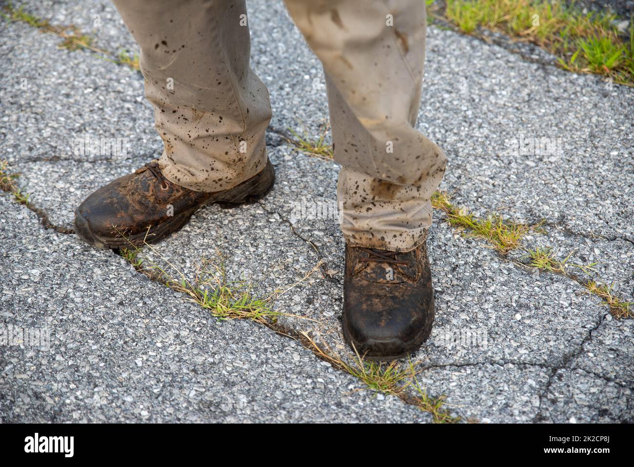 Un uomo in scarpe da lavoro e pantaloni spruzzi su strada asfaltata Foto Stock