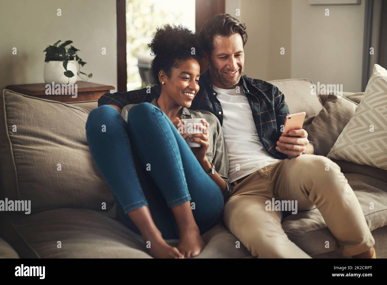 Chiudete la porta, lasciate il mondo fuori. Scatto di una giovane coppia felice utilizzando un tablet digitale mentre si rilassa su un divano nel salotto di casa. Foto Stock
