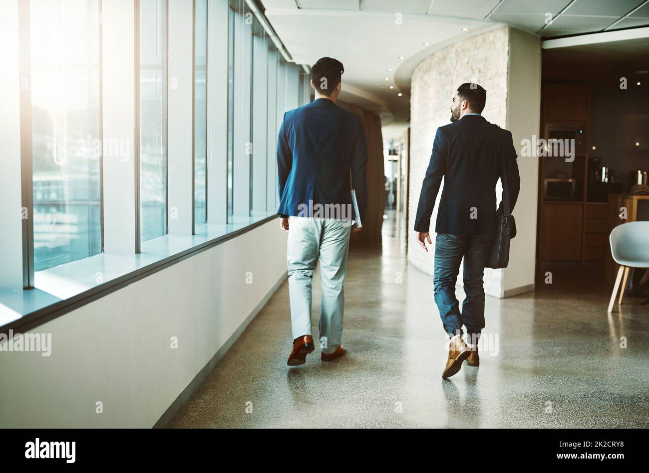 Successo doesnt accadere fino a quando la gente ottiene muoversi. Dietro l'inquadratura di due giovani uomini d'affari che camminano lungo un corridoio di un ufficio moderno. Foto Stock