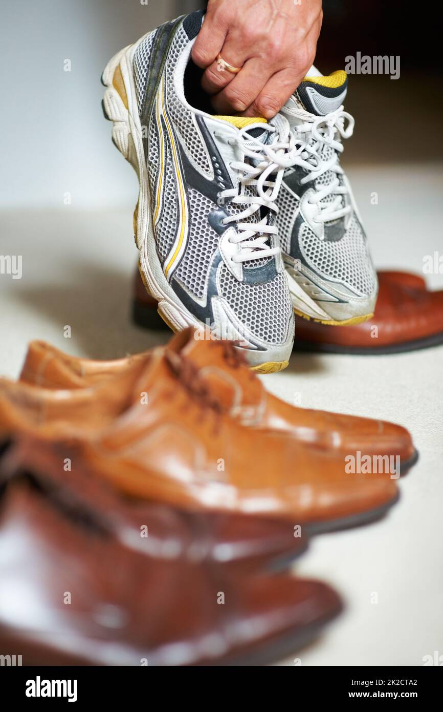 Scarpe per ogni occasione. Scatto corto di un uomo che afferra le sue scarpe da running tra le sue scarpe formali. Foto Stock