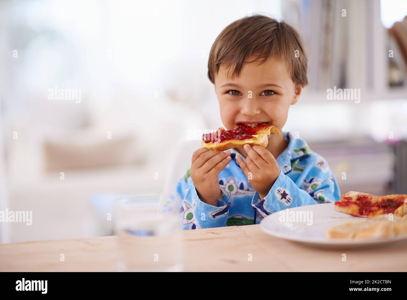 Niente è migliore di una buona colazione. Un ragazzino carino che mangia toast con marmellata. Foto Stock
