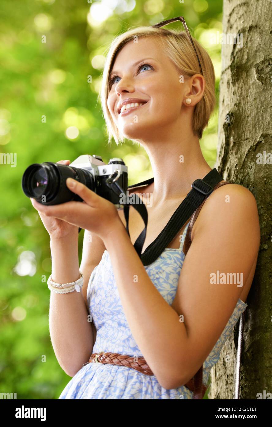 Godendo scattare alcune foto. Carino giovane fotografo che tiene la sua macchina fotografica e si appoggia contro un albero. Foto Stock