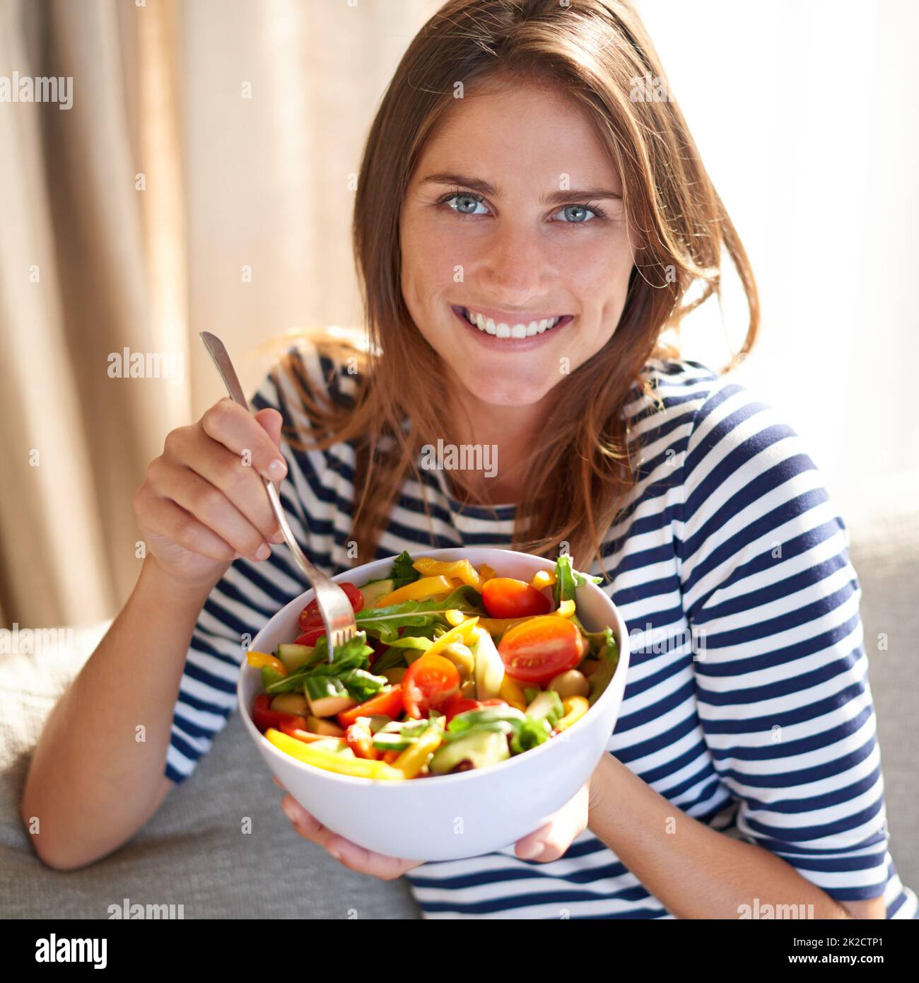 Una vita sana inizia ora. Shot di una giovane donna che mangia una ciotola piena di insalata sul suo divano a casa. Foto Stock