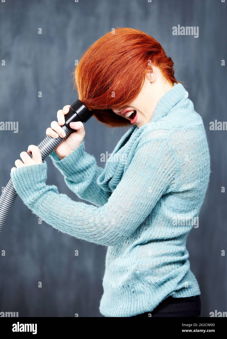 Avere una giornata di capelli cattivi. Una giovane redhead con i capelli incastrati nell'aspirapolvere. Foto Stock