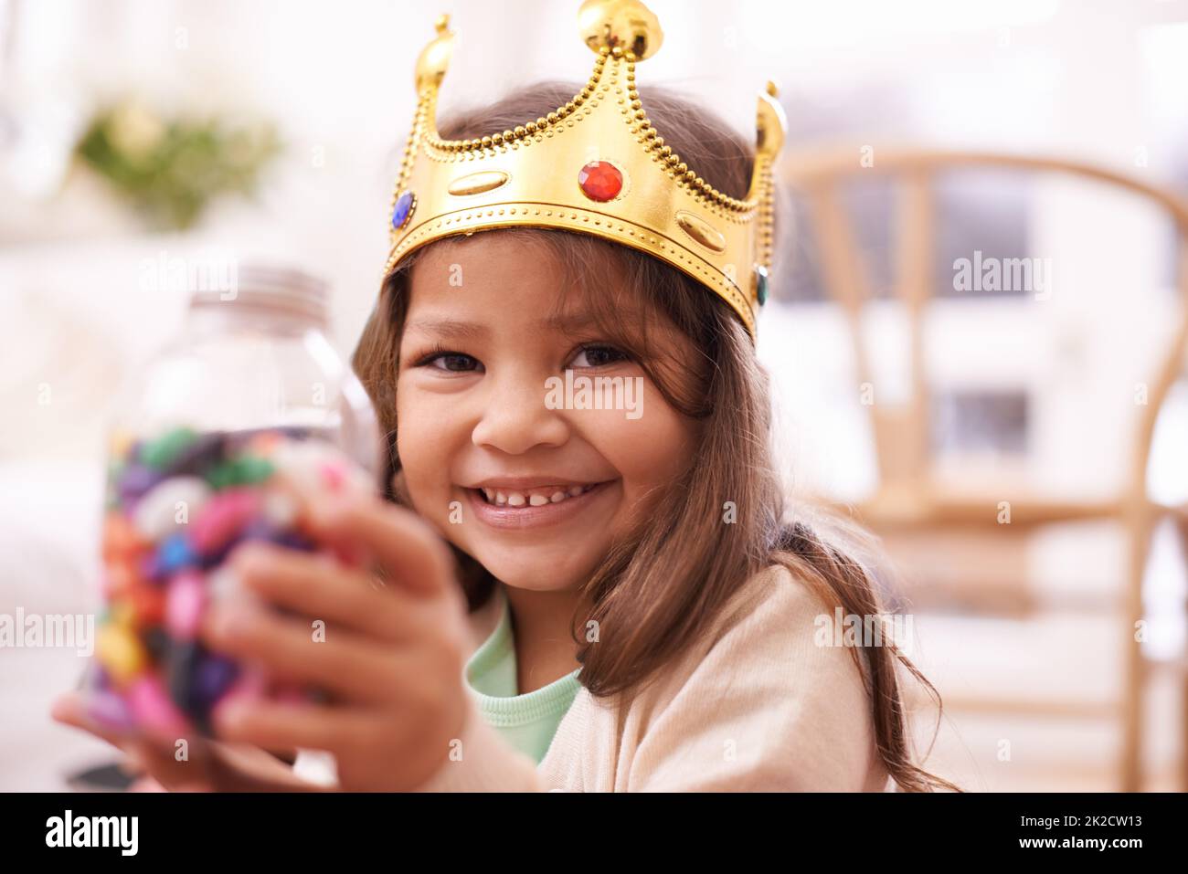 Regina della sua immaginazione. Una ragazza piccola carina vestita come una principessa mentre mangiava caramelle a casa. Foto Stock