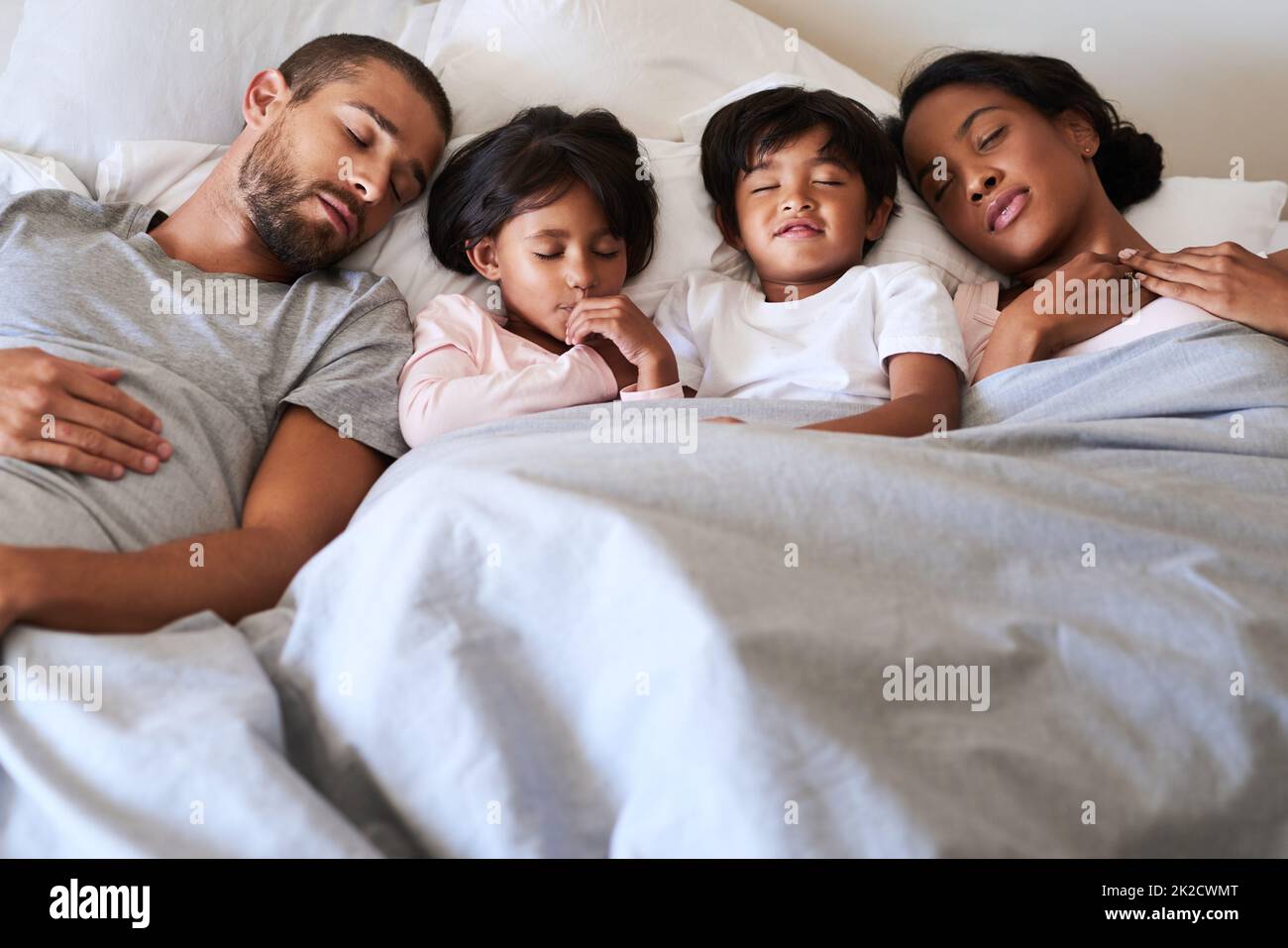 La nostra famiglia è un sogno che si realizza. Scatto di una bella famiglia giovane di quattro addormentati velocemente a letto insieme nella loro camera da letto a casa. Foto Stock