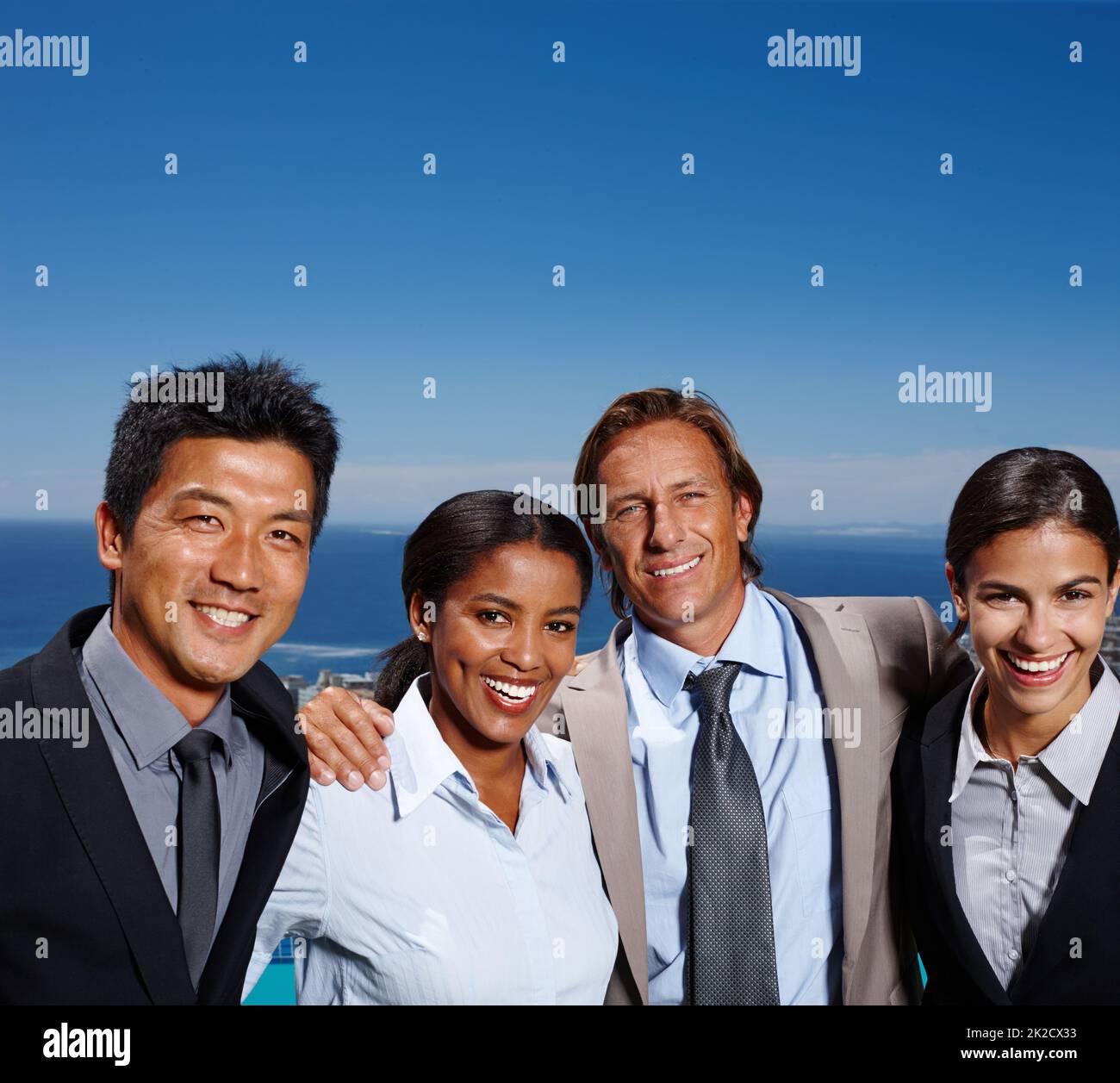 Sentirsi come theyre in cima al mondo. Scatto di quattro uomini d'affari che sorridono al sole con l'oceano dietro di loro. Foto Stock
