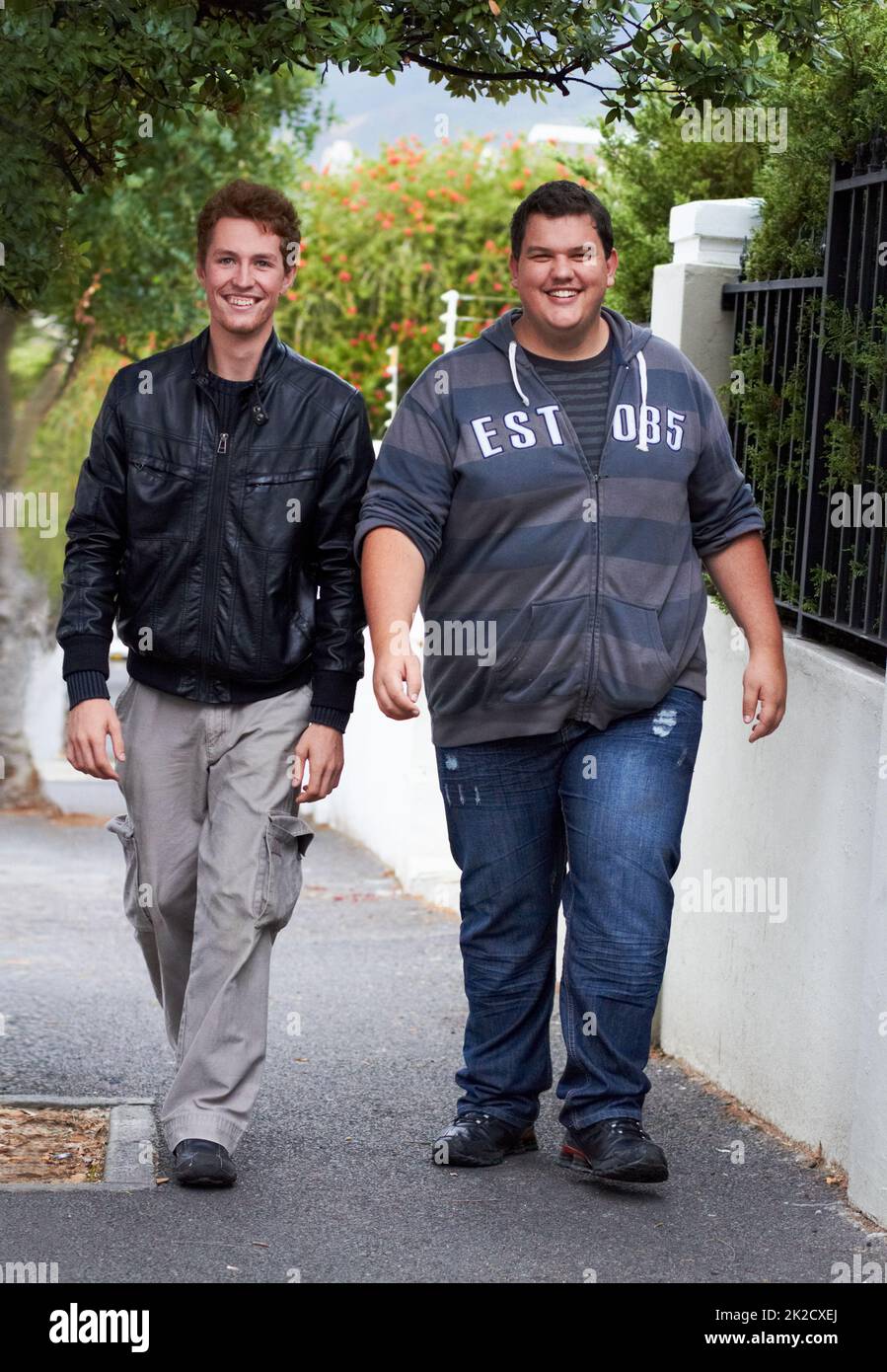 Fare una passeggiata informale. Un giovane uomo in sovrappeso vestito casualmente che cammina lungo il marciapiede con il suo amico. Foto Stock