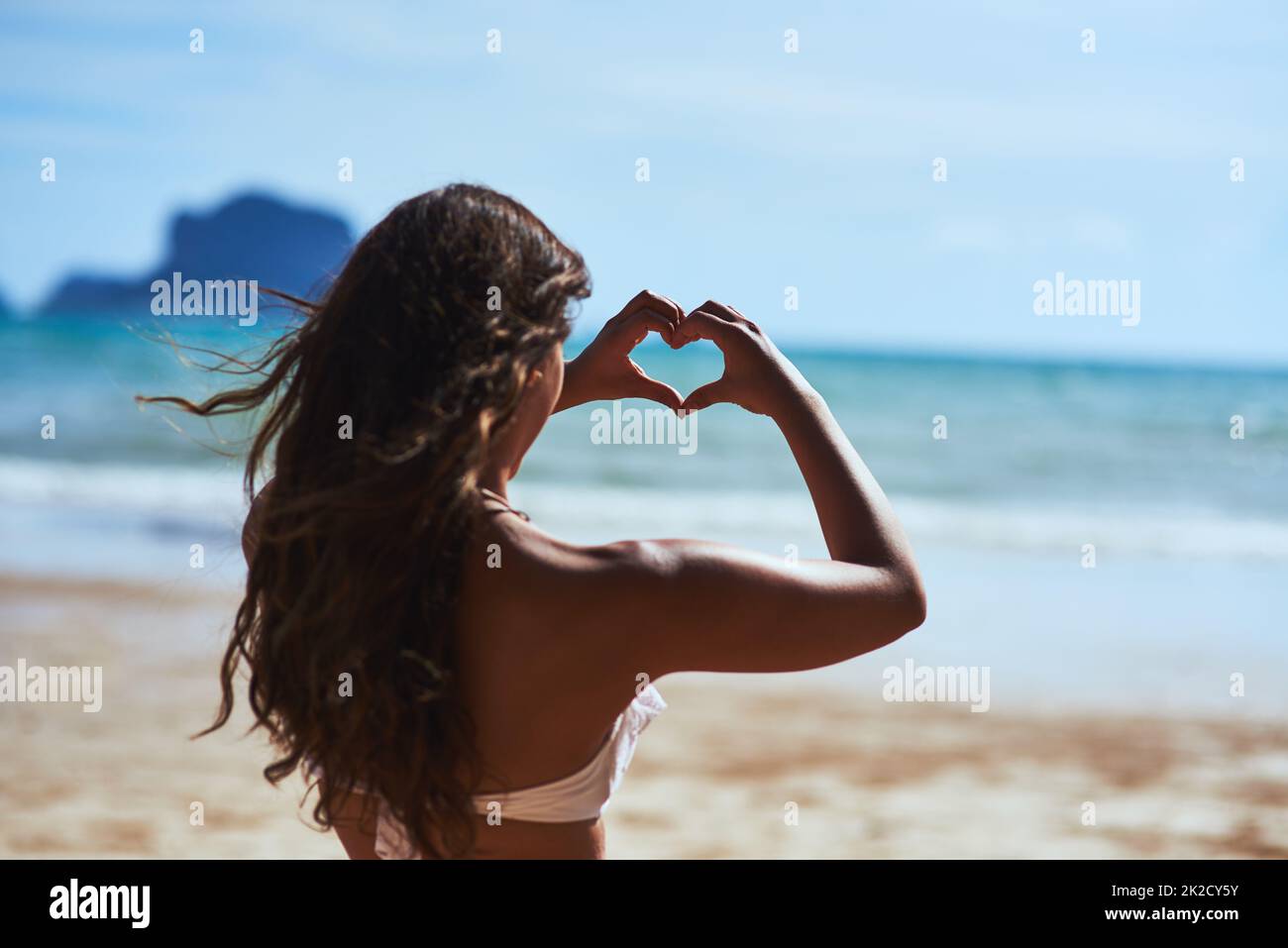 Mi piace solo la spiaggia. Scatto di una giovane donna che forma un cuore guardando il paesaggio sulla spiaggia. Foto Stock