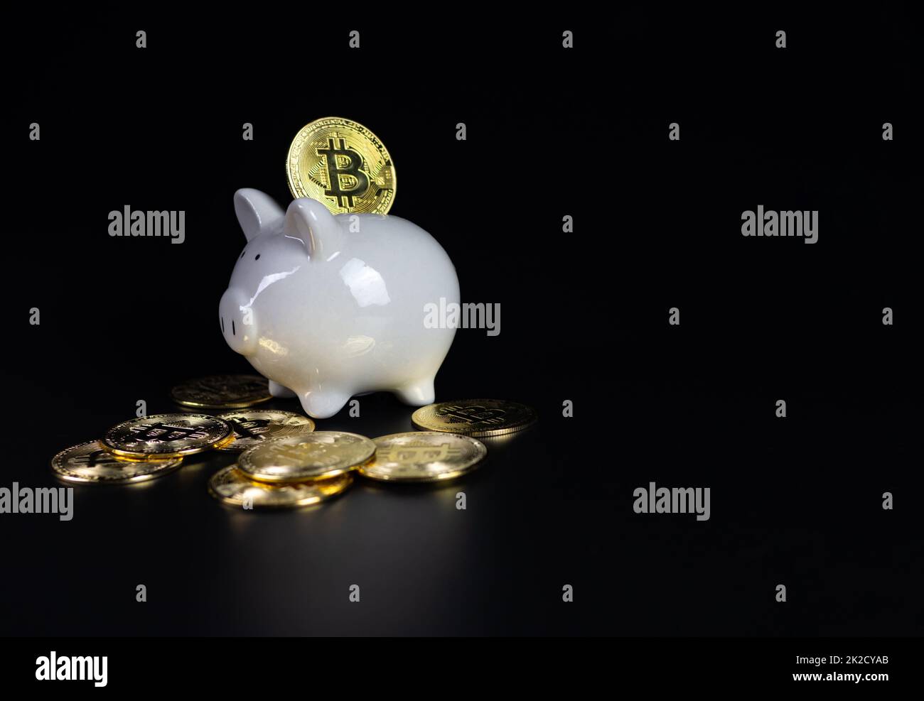 Le monete Bitcoin si trovano sul retro di una banca di porcellini bianchi, su sfondo nero Foto Stock