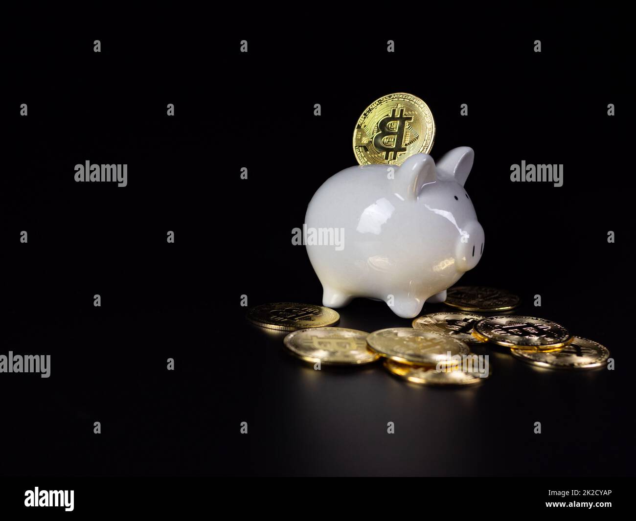 Le monete Bitcoin si trovano sul retro di una banca di porcellini bianchi, su sfondo nero Foto Stock