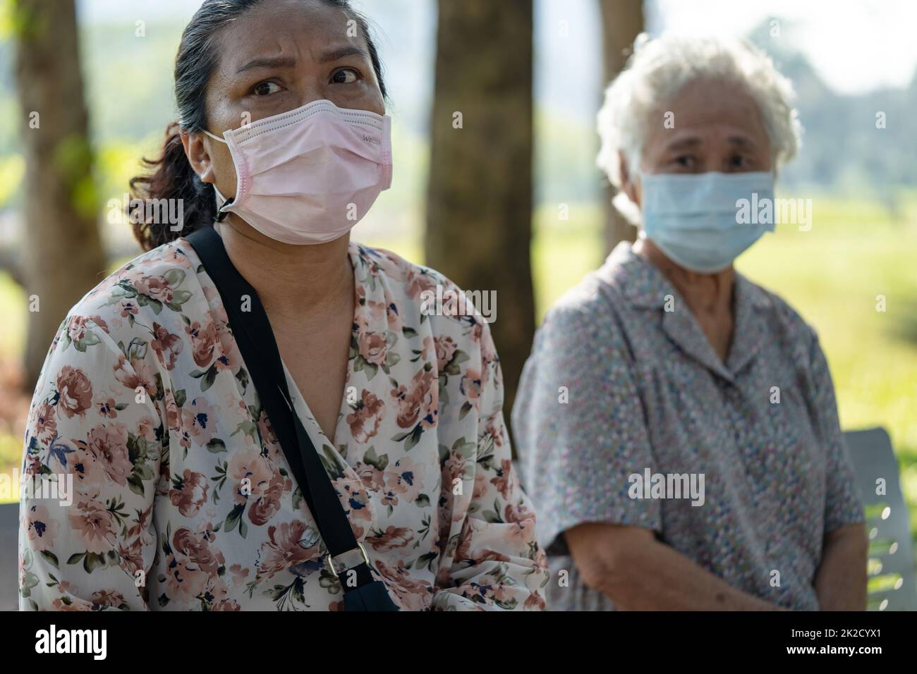 Asian anziano donna e figlia in sociale distanziamento seduta panca e indossare maschera viso per proteggere l'infezione di sicurezza Covid 19 Coronavirus in parco. Foto Stock