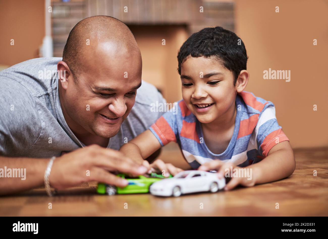 I ragazzi amano le loro auto. Scatto corto di un bambino allegro e suo padre che gioca con le automobili del giocattolo mentre è seduto sul pavimento nel paese durante il giorno. Foto Stock